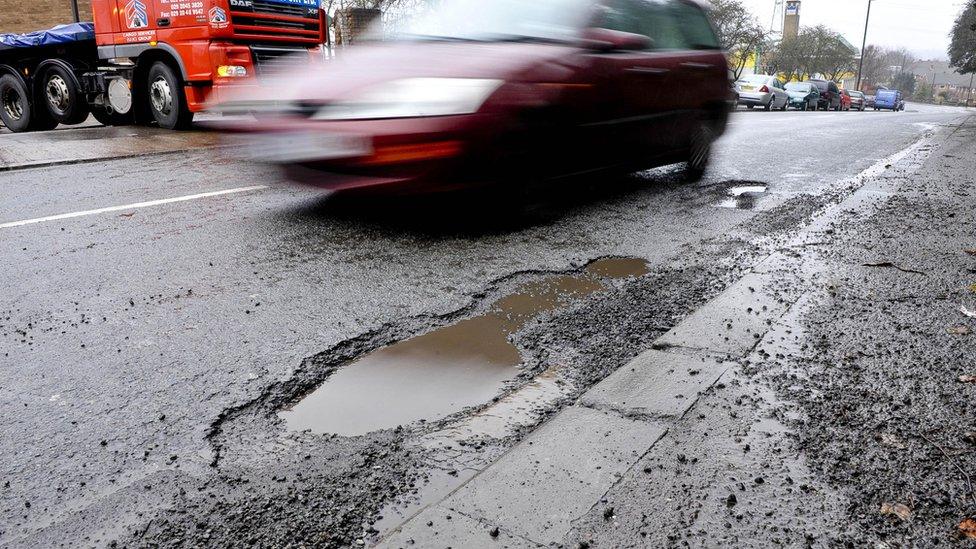 Car drives past a pothole