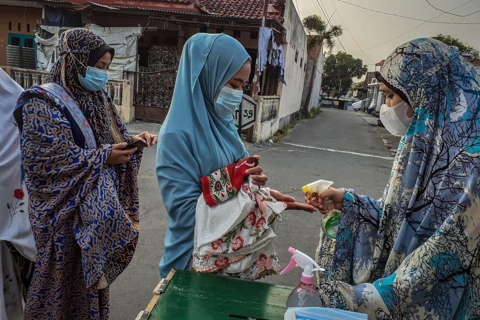 A woman sprays hand sanitizer on to the hand of another woman before Eid al-Fitr prayers in Yogyakarta, Indonesia