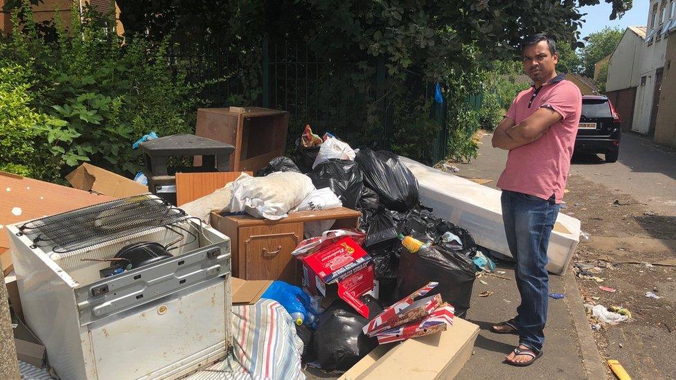 Cllr Enam Haque stood by a pile of rubbish on a street in Northampton.