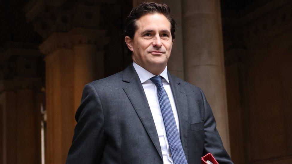 Johnny Mercer walks through a passageway wearing a suit with a blue tie