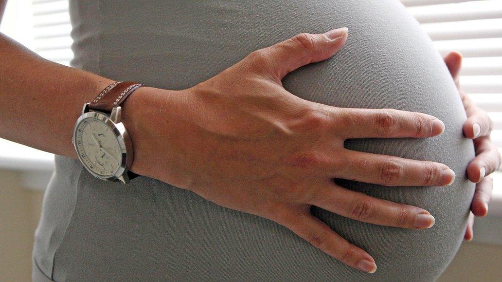 Pregnant woman holding her stomach, eight months into her pregnancy.