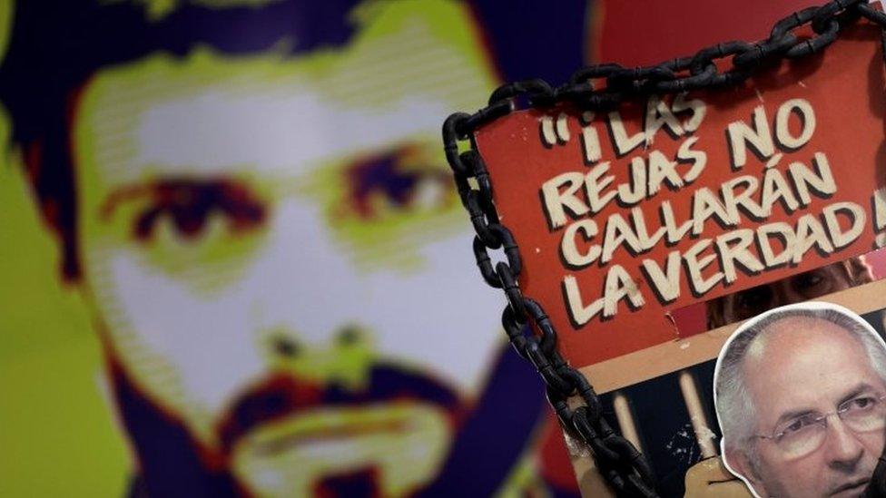 A man holds a sign with a portrait of opposition leader Antonio Ledezma in front of a wall with a portrait of opposition leader Leopoldo Lopez during a news conference