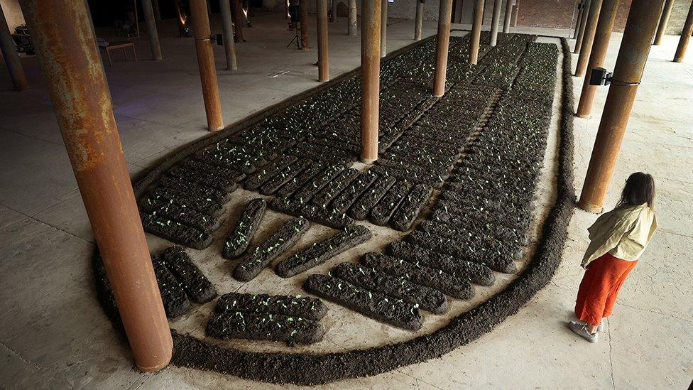 A woman looks at "Chorus of Soil' a work by Italian artist Binta Diaw which is a large-scale reproduction of the shape of the slave ship 'Brooks' constructed from seeds and soil