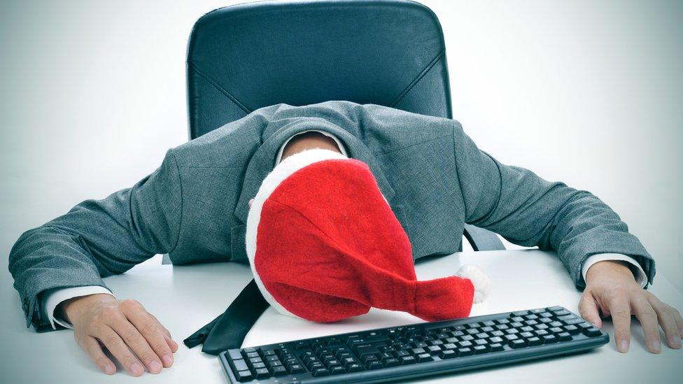 Man in Santa hat rests head on desk.