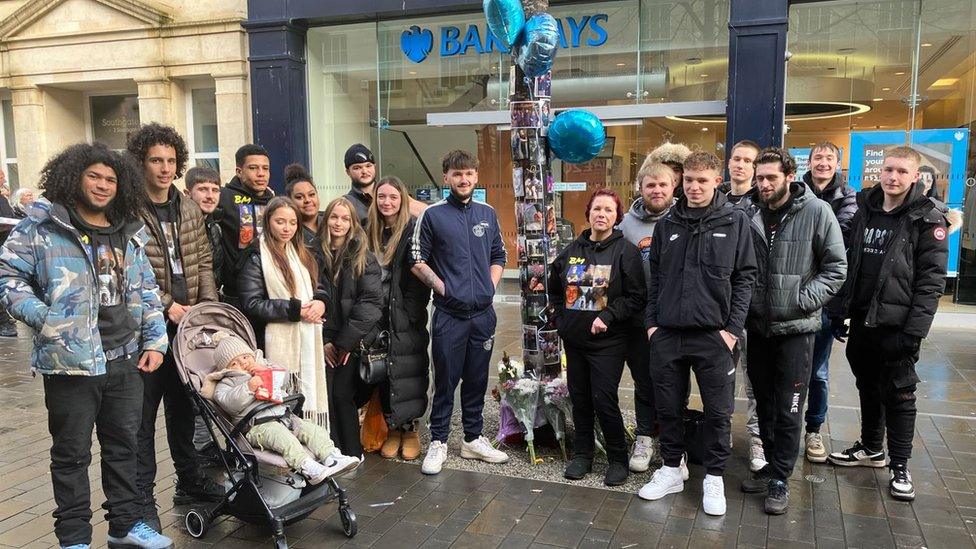 Ben's family stood in front of the tree with pictures and balloons