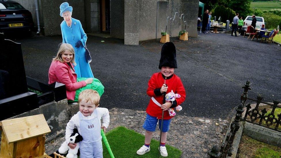 Laura McKnight holds a cardboard cut-out of Queen Elizabeth II as her sons Noah (5) and Louis (2) play mini golf at a picnic at St Bartholomew's Parish Church, Newry, as part of the Big Jubilee Lunch