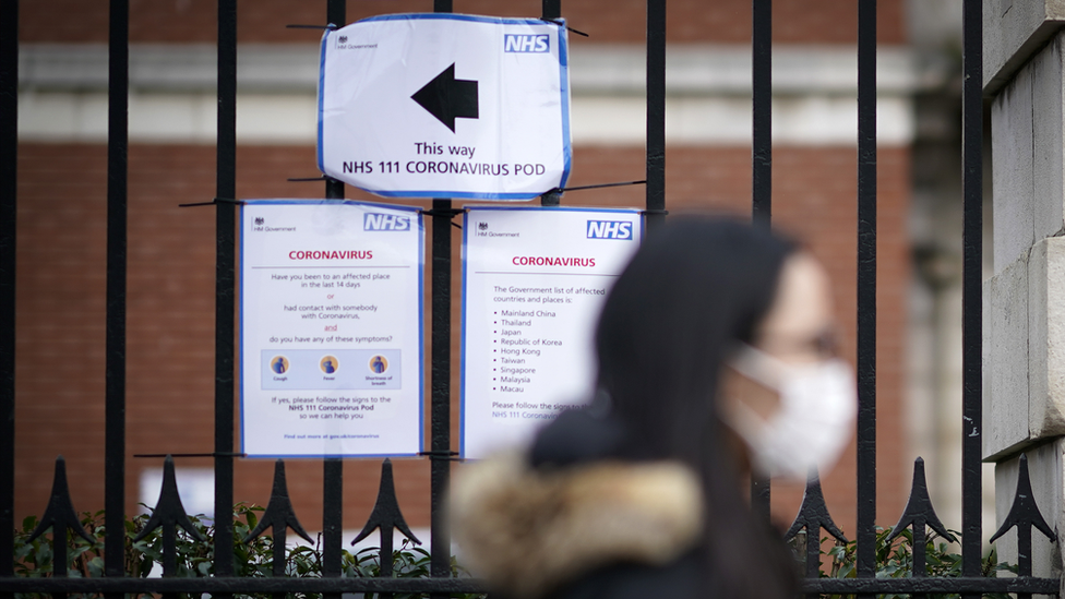 A person wearing a protective face masks walk past a direction sign to COVID-19 coronavirus isolation pods at Manchester Royal Infirmary