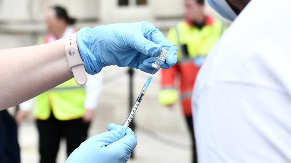 A pair of hands wearing surgical gloves drawing the Covid-19 vaccine from a vial