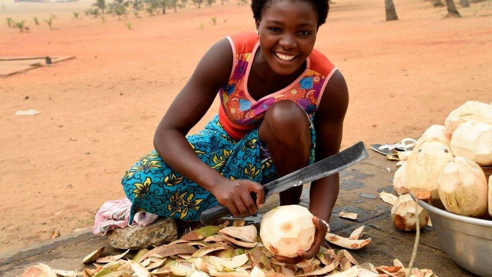 A woman tries to remove the outer coating of a coconut shell, to sell along the Road in Lome, Togo on February 12, 2020