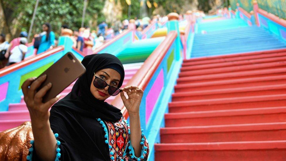 A woman takes a selfie in front of the staircase leading to the Batu Caves temple complex in Kuala Lumpur