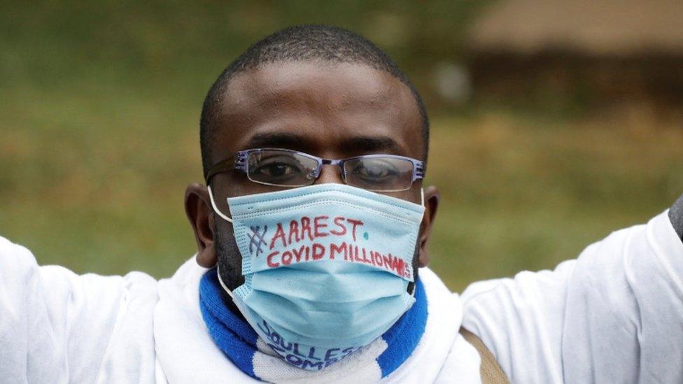 A protester wears a mask which reads: "Arrest Covid millionaires"