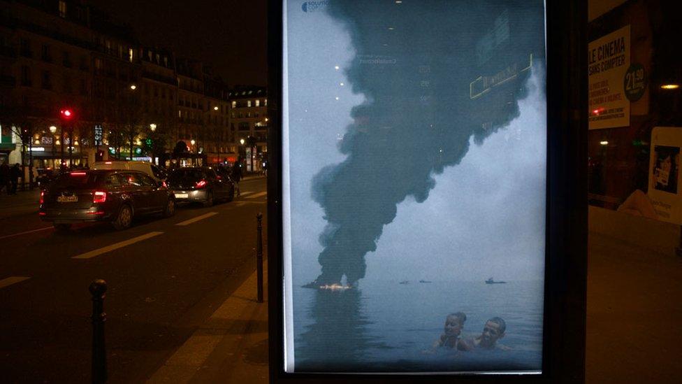 US President Barack Obama shown swimming in the ocean as a fire rages in the background and black smoke rises from the water.