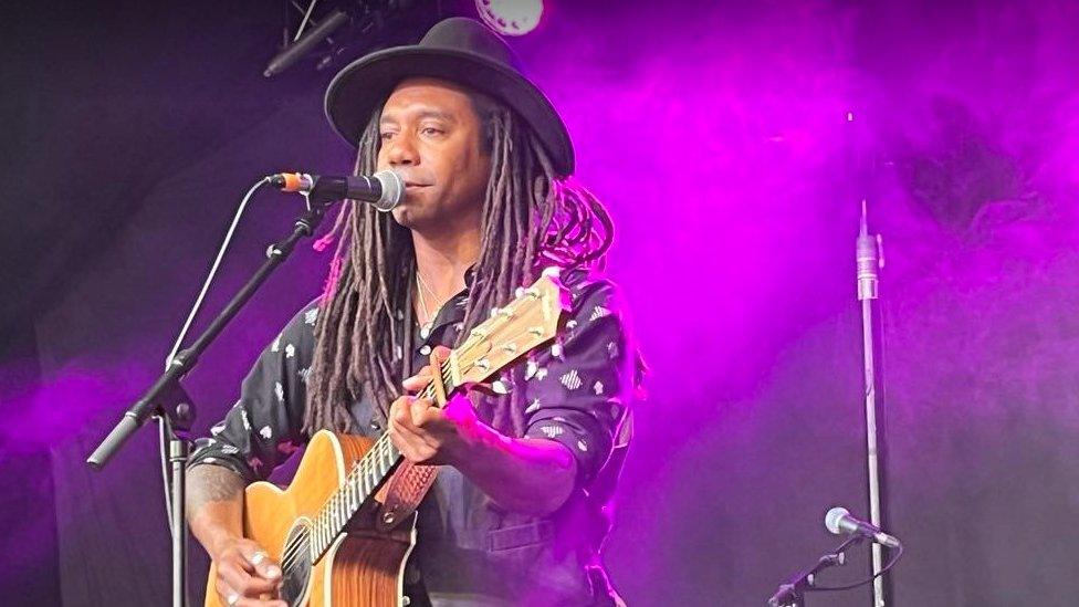 Julian Taylor wearing a black shirt and hat, playing the guitar