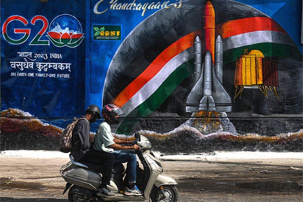 A man on his bike moves past a wall mural surrounding a garbage dump beside a G20 Summit Logo, ahead of the G20 Summit in New Delhi, India on September 6, 2023. India will host the 18th G20 Summit from September 9-10 in New Delhi.