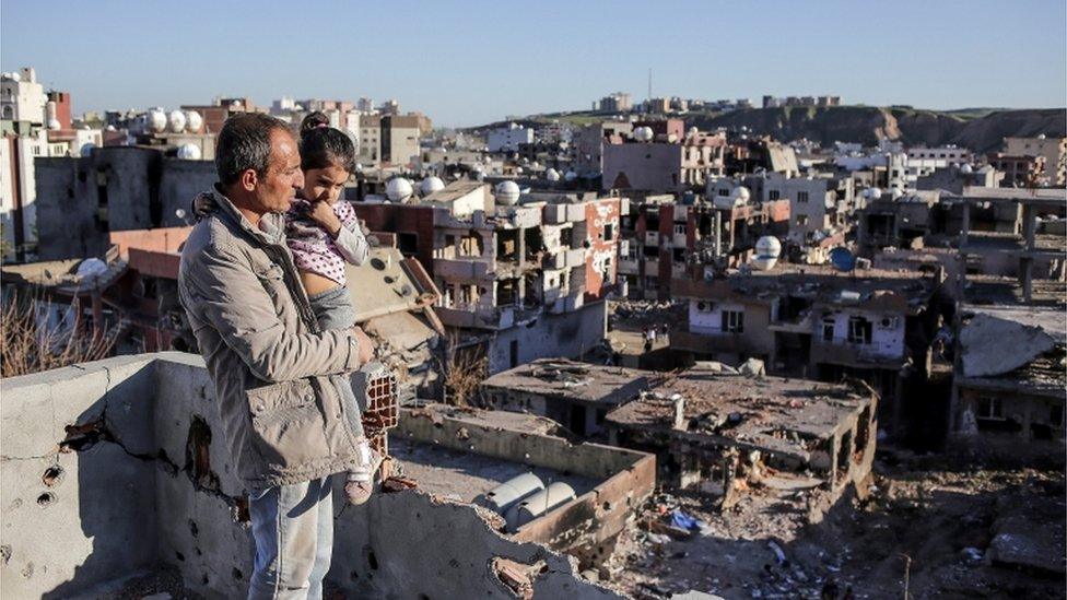 A man holds his daughter as he looks out at the ruined houses of Cizre, 2 March 2016, Turkey