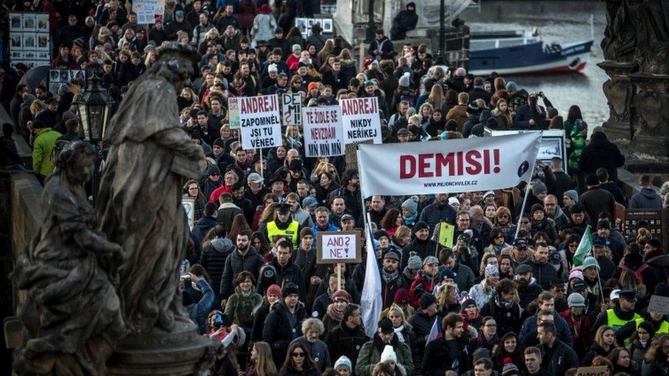 People carry a banner reading "Resignation" as thousands of demonstrators march on the Charles Bridge to protest against Czech Prime Minister Andrej Babis