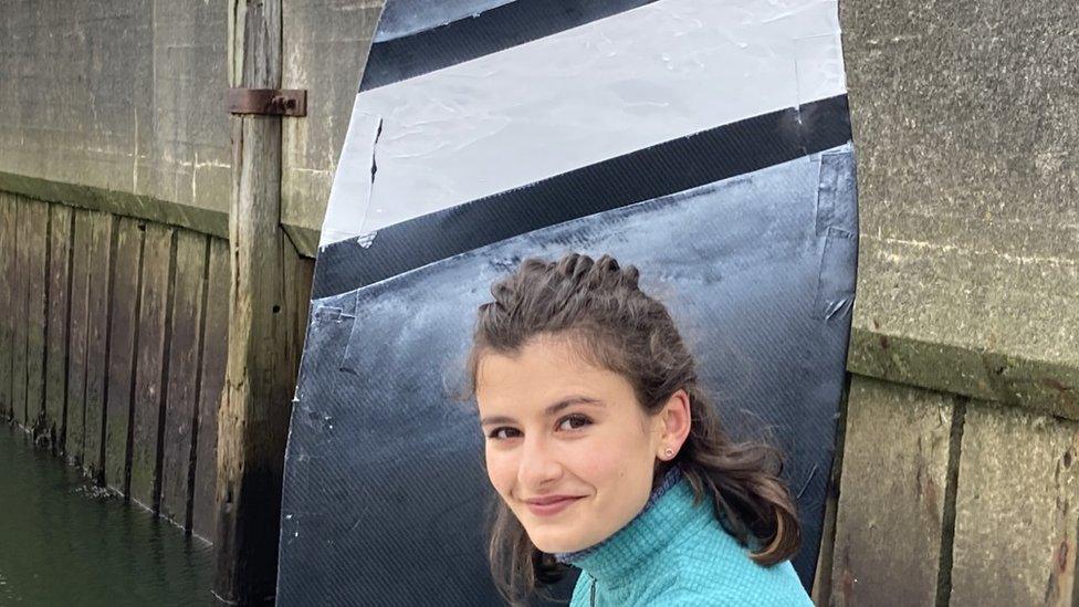 Anahita Laverack standing in front of black flat sail with a white stripe