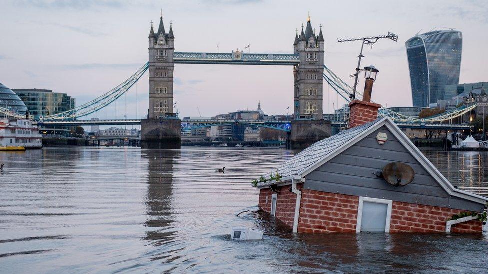 A replica of a British house floats in front of Tower Bridge on the river Thames