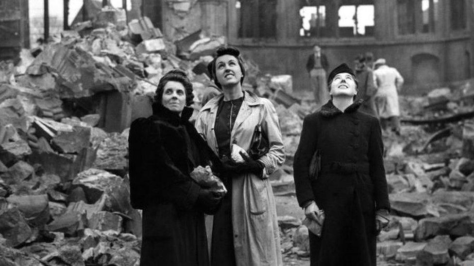 Three women stand in the rubble