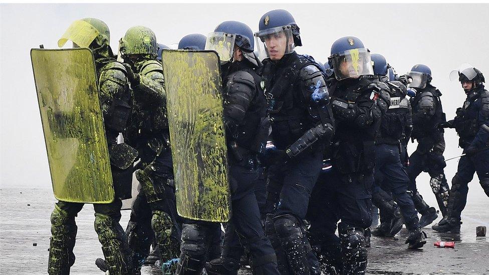 Riot police carry shields covered in yellow paint during protests in Paris on 1 December 2018