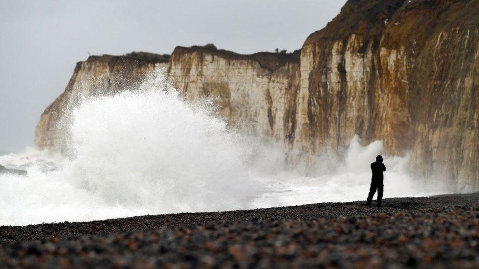 high waves crashing along a beach with cliffs in background and person in black looking out