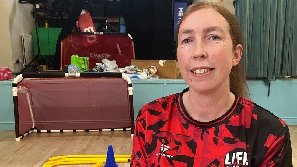 A woman sits in a hall surrounded by sports equipment