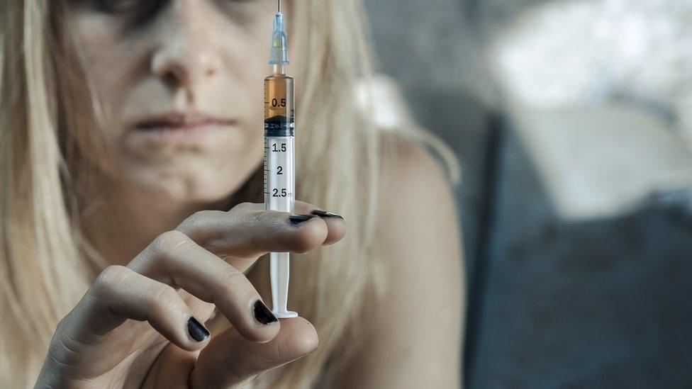 Stock photo of drug addict holding up a syringe with a brown liquid in