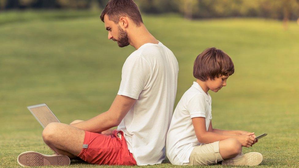 Dad and son playing with digital gadgets back-to-back