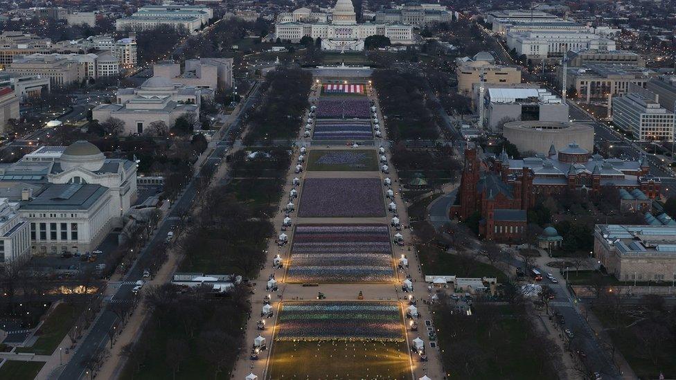 The Whitehouse in the distance in front of many flags laid on the ground.