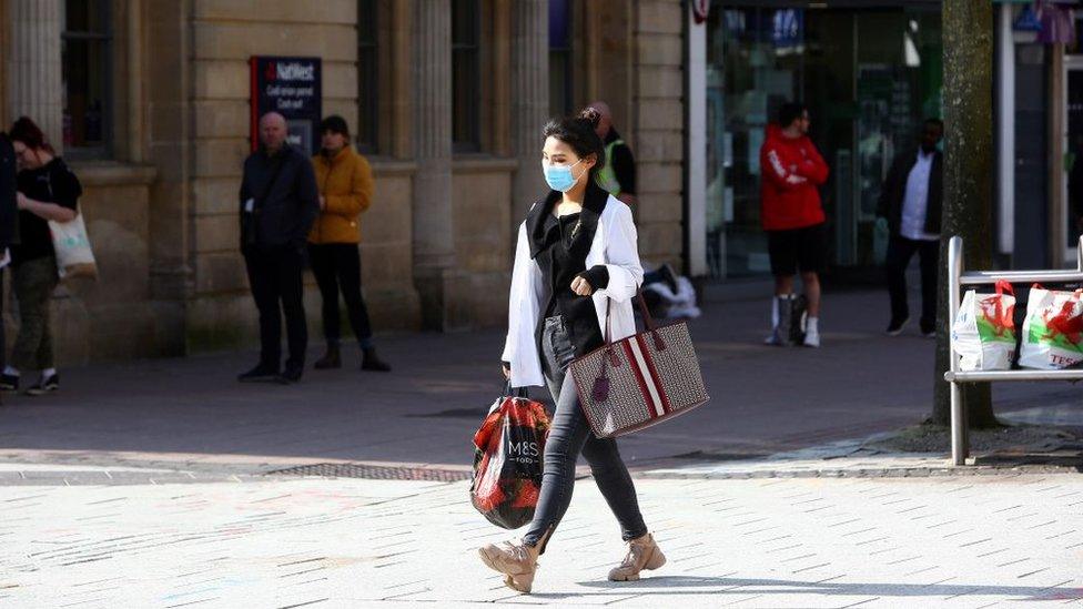 A woman, wearing a face mask as people stand at a distance and queue to enter a bank in Cardiff in March 2020