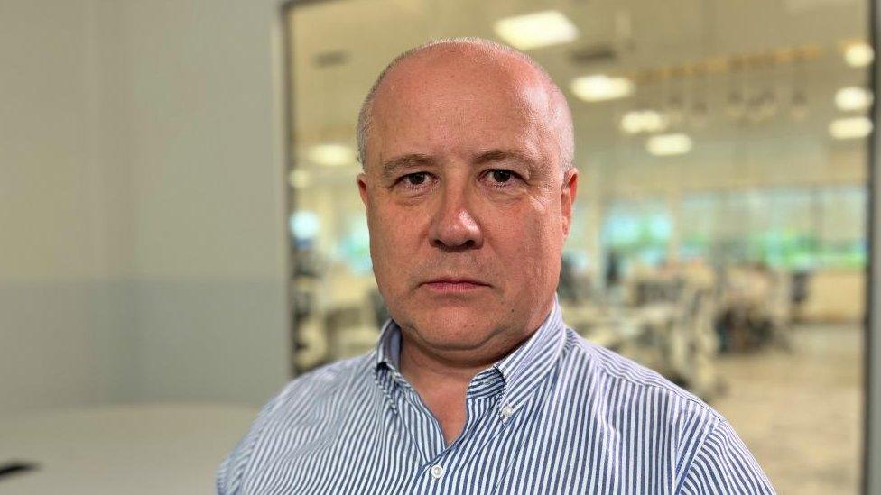 Man with very short hair and stripped shirt in a large office building