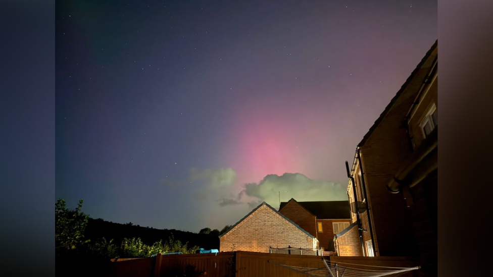 A shot of the pink aurora above a lit up house in Ceredgion