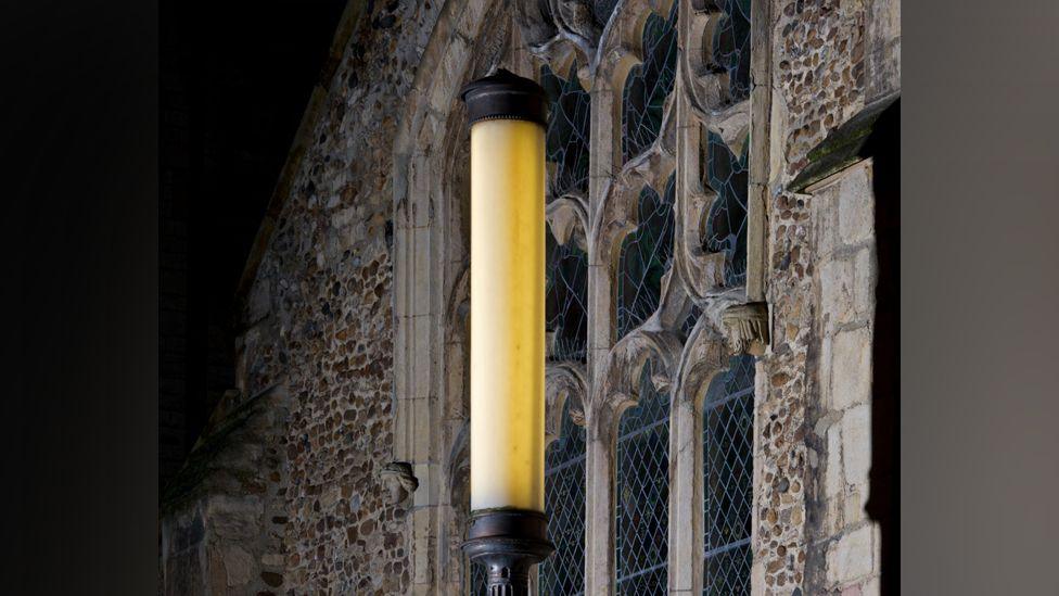 A lantern lit up outside an ornate church window in Cambridge