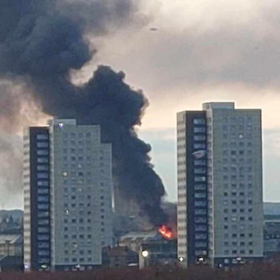 Fire and smoke visible, with two high-rise blocks in the foreground.