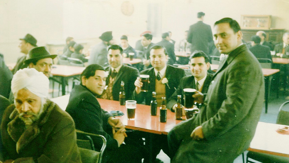 Archive photo of Avtar Singh Jouhl on the right with a group of five other men clustered around a table with pints and bottles of beer. It looks like a working men's club in the 1960s