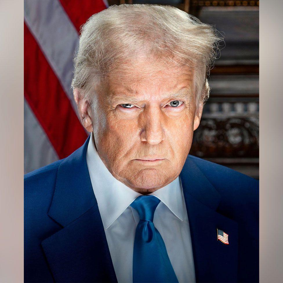 Donald Trump appears in his official presidential portrait for his second term in office. He looks directly into the camera and appears to have a raised eyebrow. He is wearing a blue tie and white shirt with an American flag lapel on the left side of his suit jacket