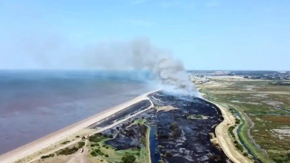 An aerial of Wild Ken Hill in Snettisham. Black charred areas are shown on the reserve which has been affected by a fire and smoke is billowing into the sky from the site.