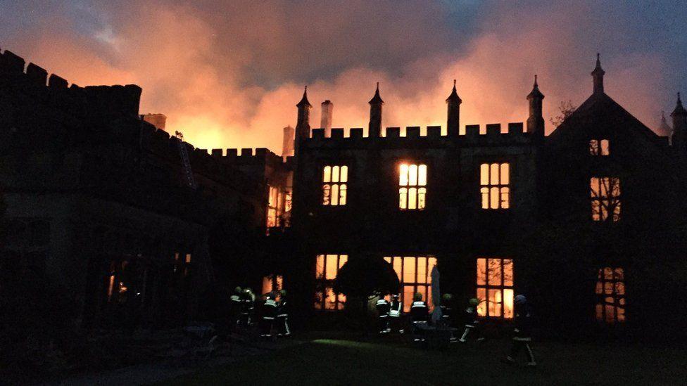 Parnham House is silhouetted by a fire which glows through ground and first floor windows and lights up clouds of smoke above the roof.