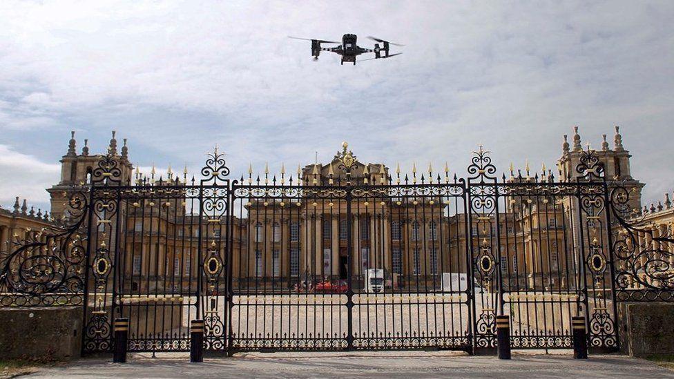 Drone hovering just above the black and gold entrance gates with Blenheim Palace in the background