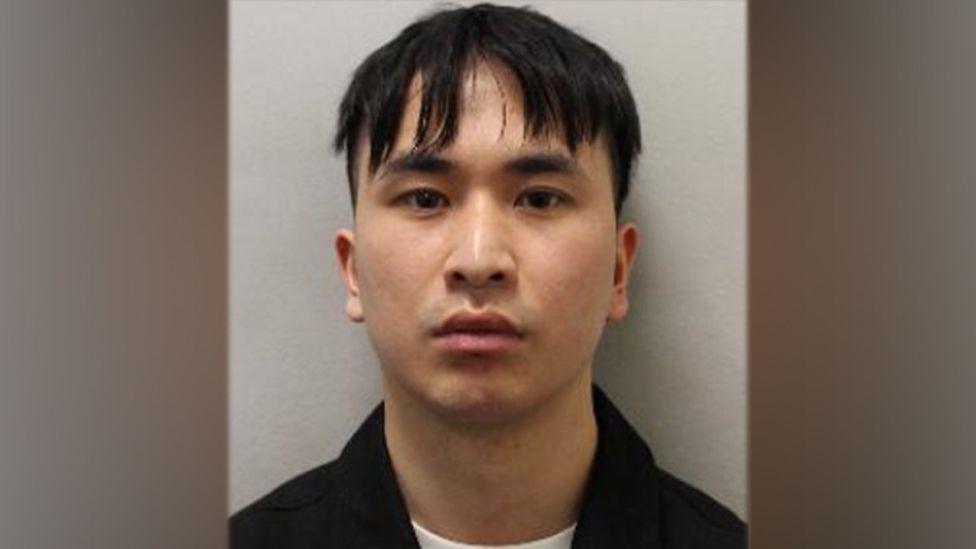 A man with dark hair and a fringe stares into the camera. It is a police mugshot. 