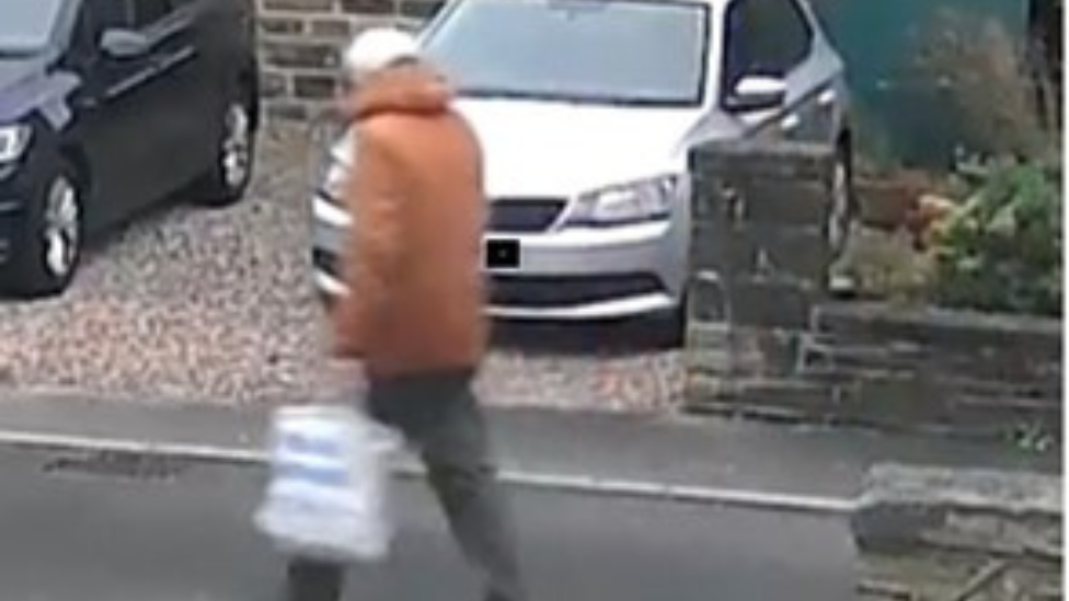 CCTV image of a man in an orange jacket, carrying a plastic bag, walking along a residential road