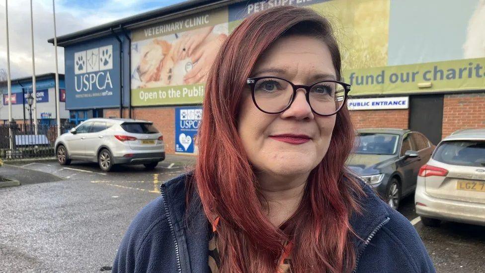 Siobhan McHaffie wearing a blue fleece and black glasses, with red hair, stood outside a USPCA building