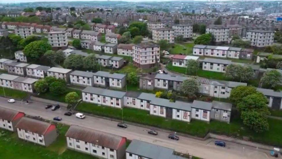 Aerial view of rows of houses and flats, with cars on roads.