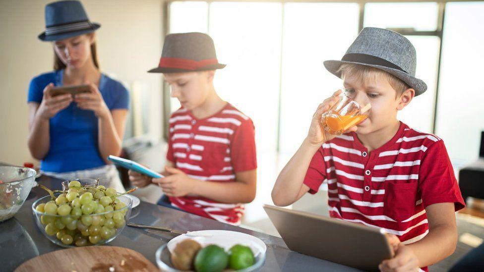 Children in a family home using various electronic devices, including tablets and phones 