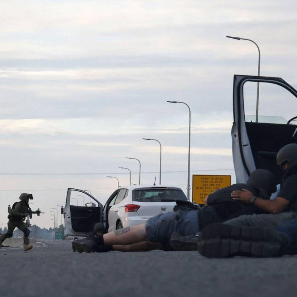 Journalists take cover behind cars as Israeli soldiers take position during clashes with Palestinian fighters near the Gevim Kibbutz, close to the border with Gaza on 7 October, 2023