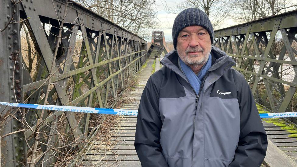 Roddy Robertson standing at the Spey Viaduct, the damaged section is visible in the distance, and there is police tape behind him.