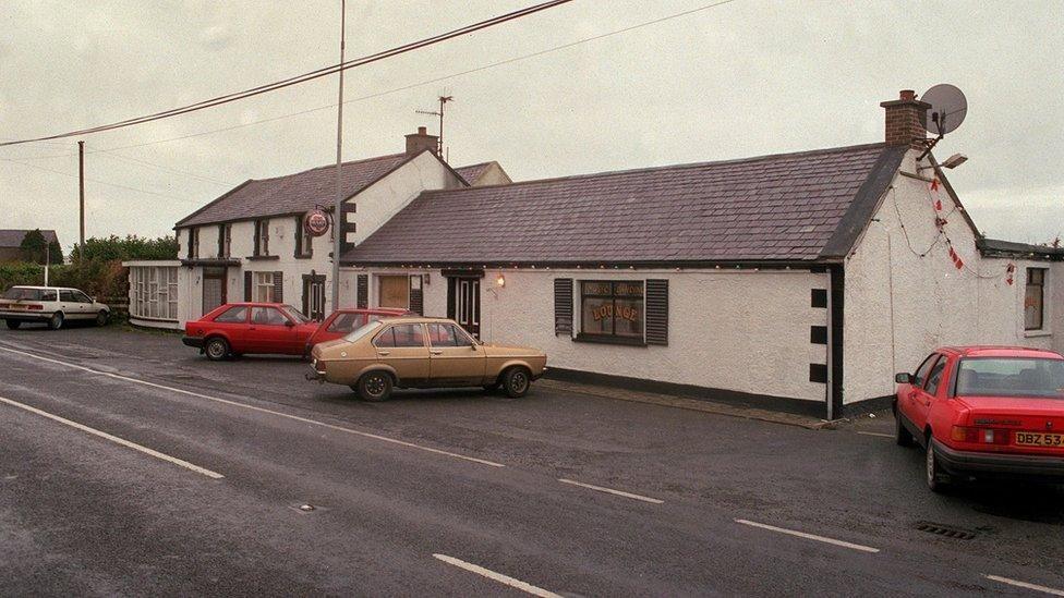 A cottage style building with white washed walls and cars from the 1990s parked outside.