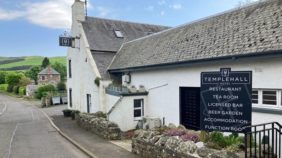 A white pub building in the Borders with a sign for the Templehall Hotel in front of it