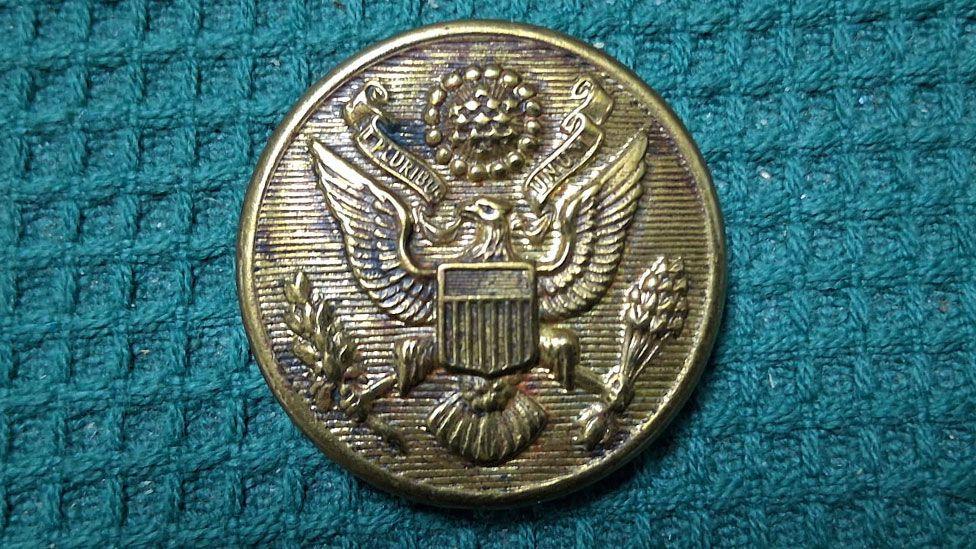 A close-up of a World War Two US Airforce button. It appears to be made of brass, is round in shape and shows an eagle with spread wings.