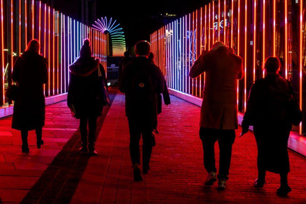 Five people walking through a bright installation.